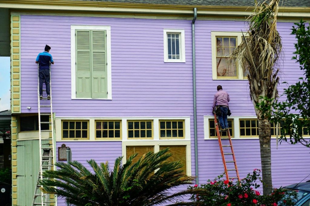 Painters on ladders repainting a two-story house